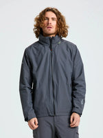 A person with curly hair is standing against a plain background, wearing the SLAM CREW WARM HOODED JACKET—a gray, waterproof jacket inspired by winter sailing jackets. The jacket features a high collar lined with polar fleece, and the person’s hands are relaxed by their sides.