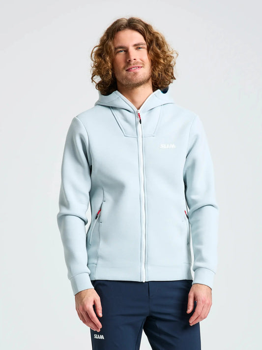 A man with curly hair wears the SLAM ACT FULL-ZIP HOODIE, crafted from stretchy scuba material with a regular fit and a subtle logo on the chest, paired with navy blue pants. He stands against a plain light background, his hands relaxed at his sides.