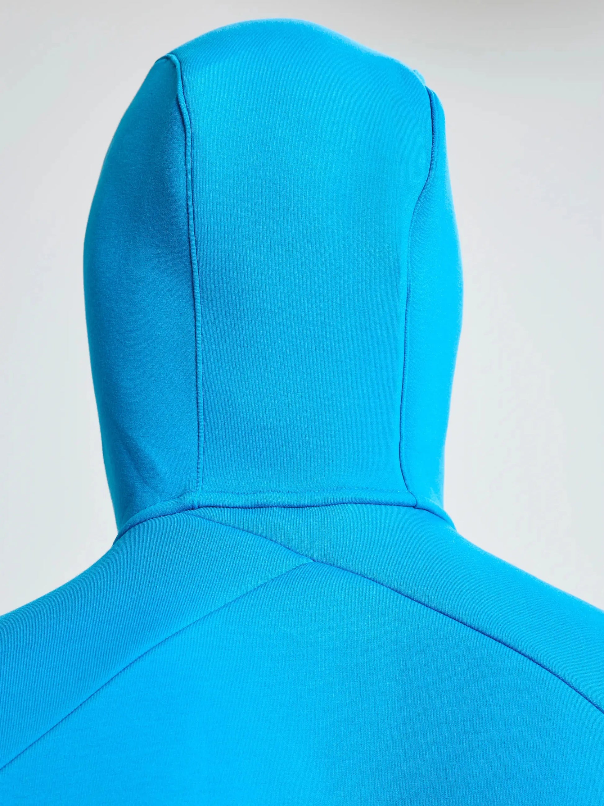 A close-up view of a person wearing the SLAM ACT FULL-ZIP HOODIE in bright blue with the hood up, highlighting the back of this regular fit garment crafted from stretchy scuba material against a plain, light background.
