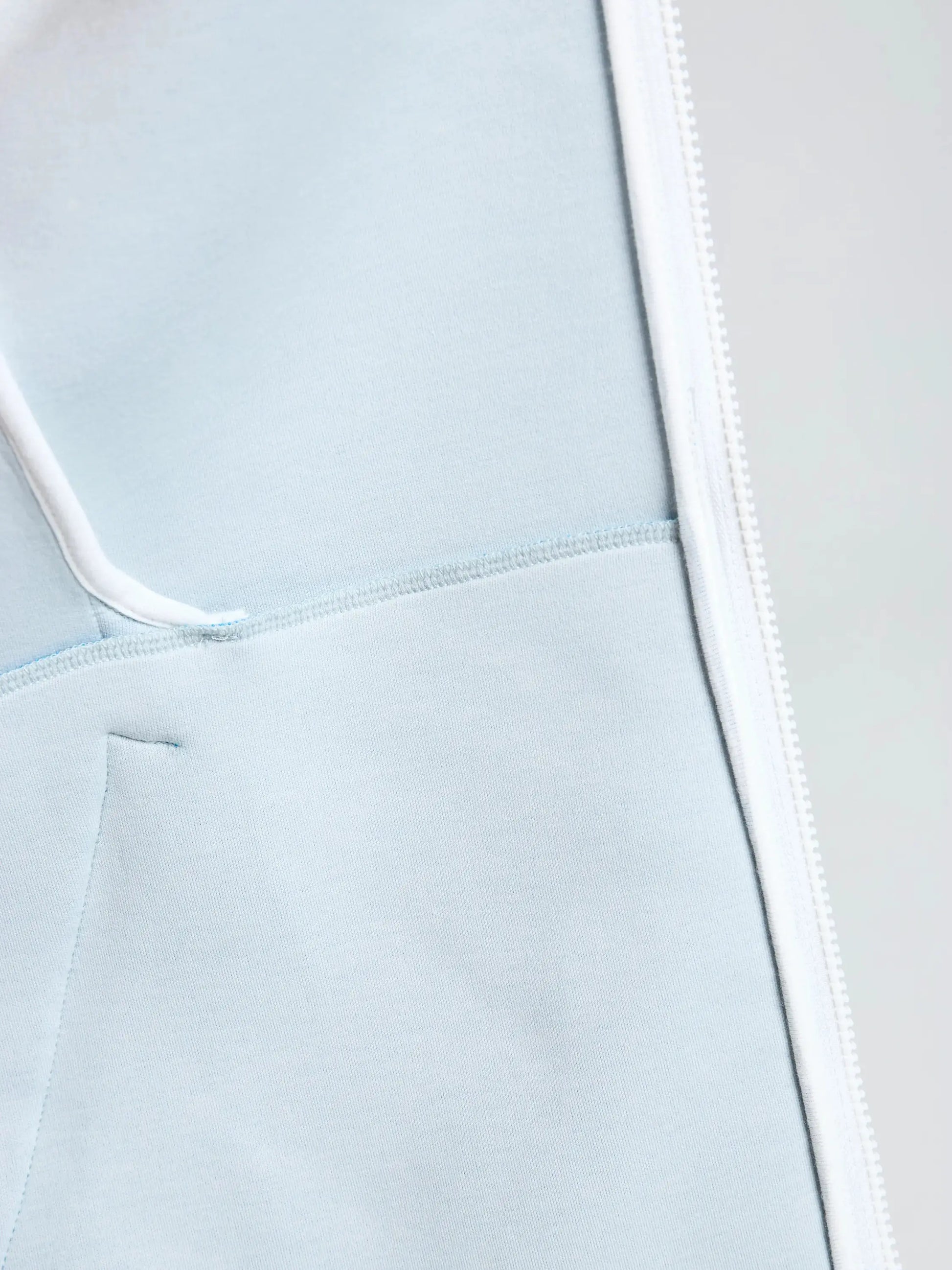 Close-up of the SLAM ACT FULL-ZIP HOODIE in light blue, made from stretchy scuba material, featuring visible stitching, a white right-side zipper, and detailed views of the seam and pocket.
