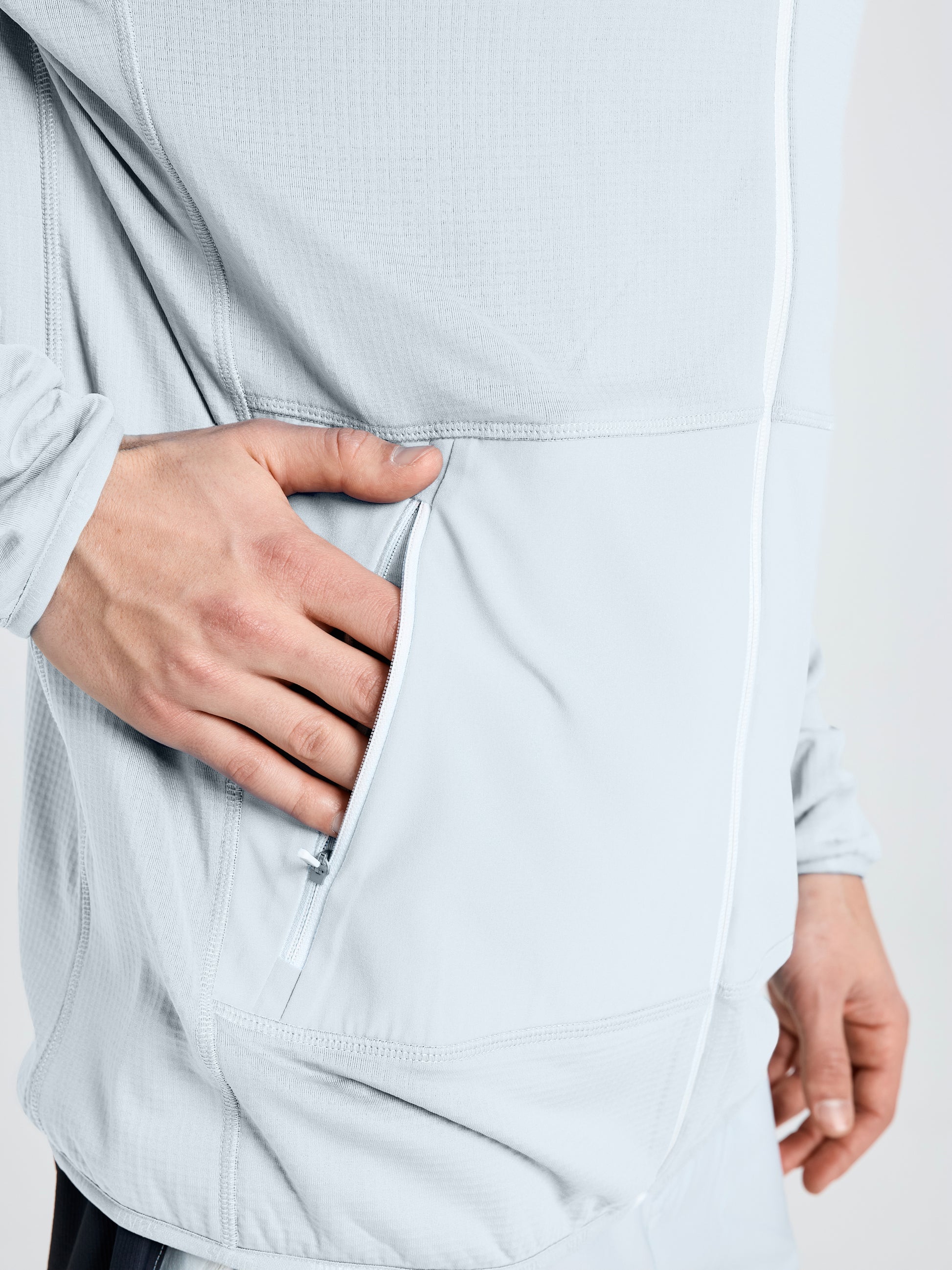 A person wearing the SLAM ALTURA FZ LGT GRID FLEECE in light gray places their left hand in a large side pocket. The image is cropped to show the torso and part of the hand.