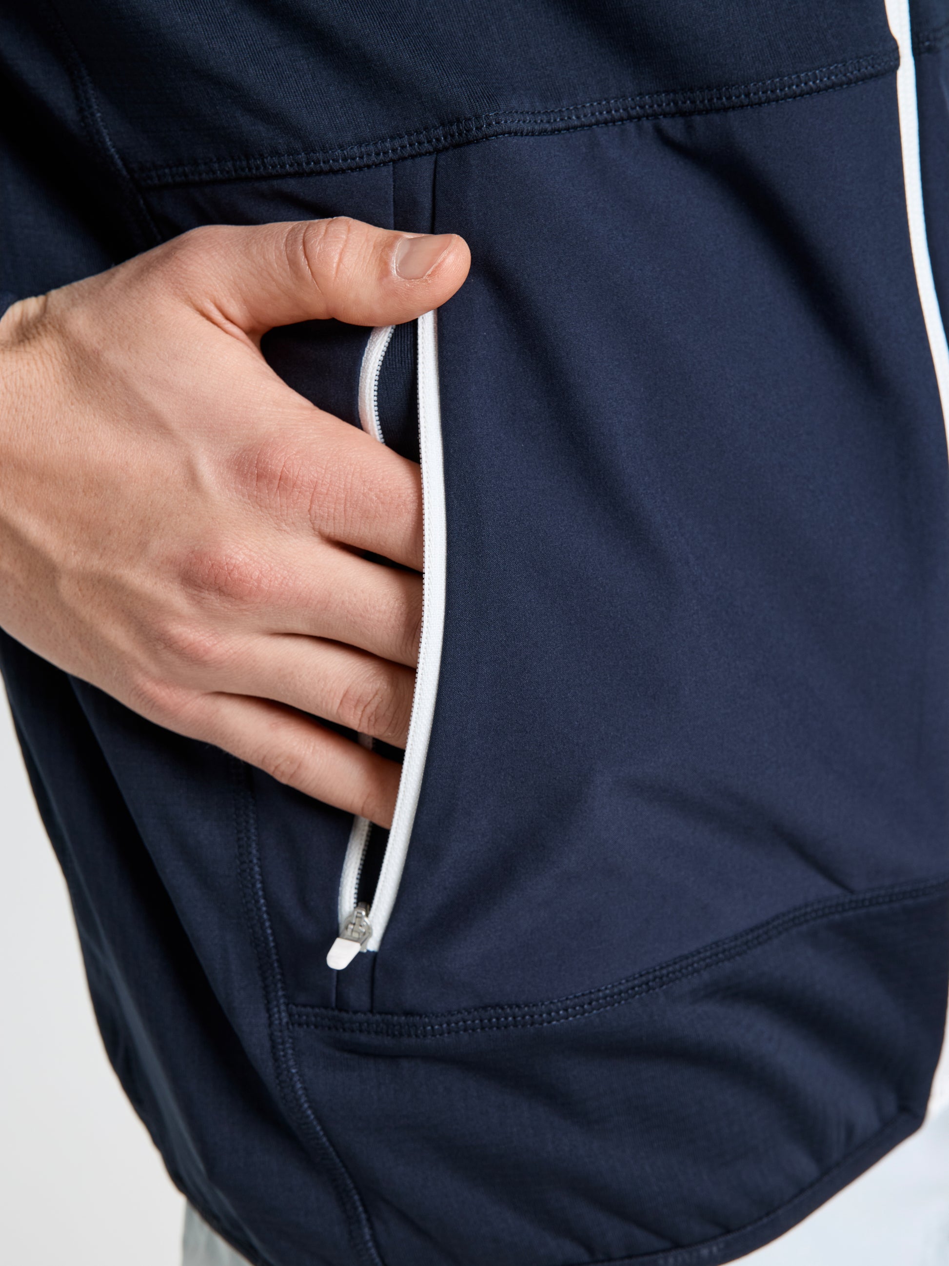 A close-up of a hand partially inserted into the zippered pocket of the SLAM ALTURA FZ LGT GRID FLEECE sailing jacket in dark blue, featuring a white zipper and crafted from lightweight technical fleece.