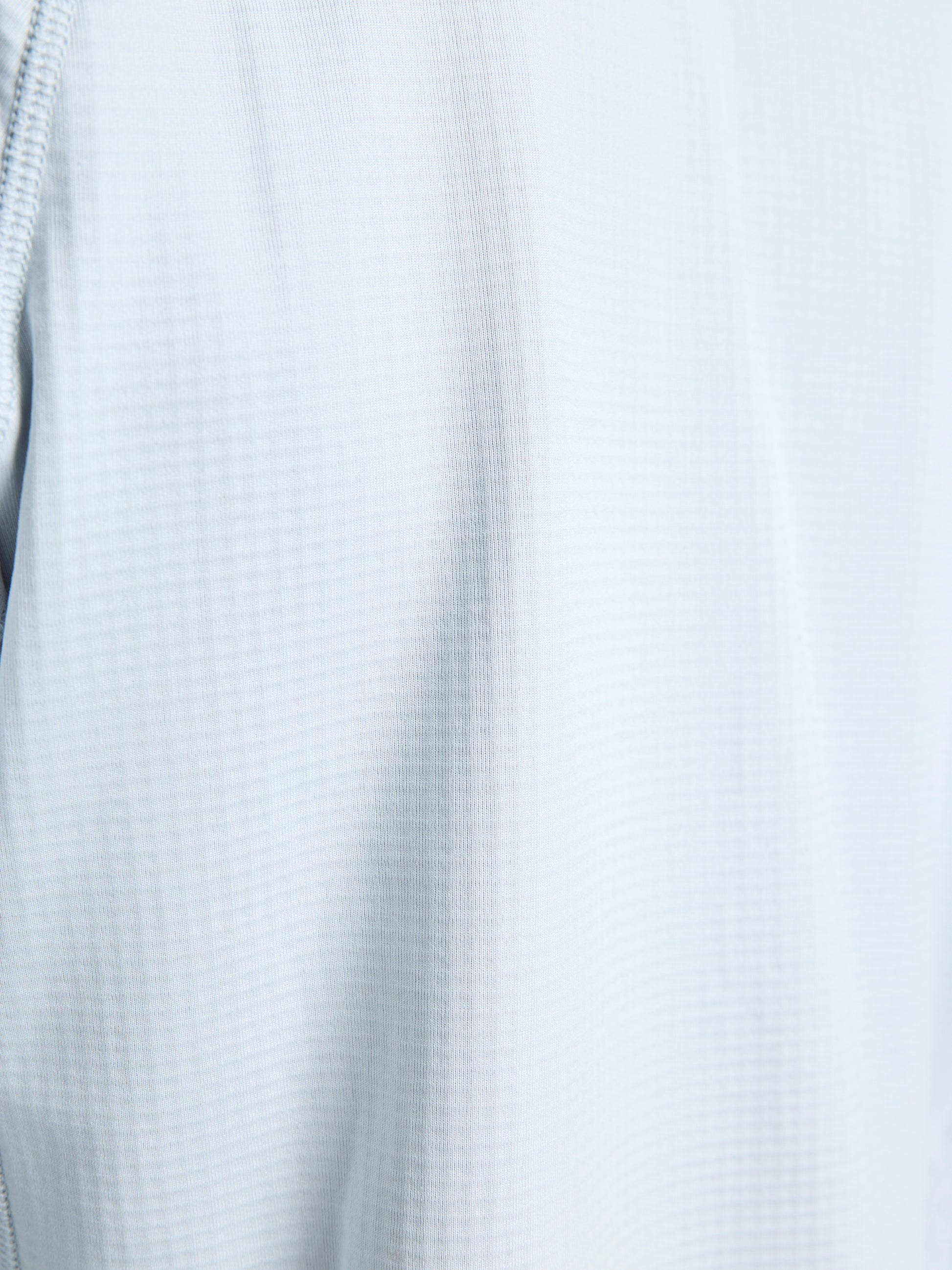 Close-up of SLAM’s ALTURA HZ LGT GRID FLEECE shows its light gray grid fleece fabric with subtle vertical ribbing and visible stitching details along the left edge.