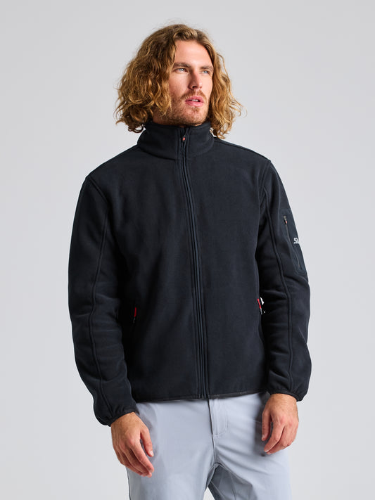 A person with long, wavy hair is wearing a DECK FLEECE jacket by SLAM in BLACK INK and gray pants. They stand against a neutral background, looking slightly to the side.