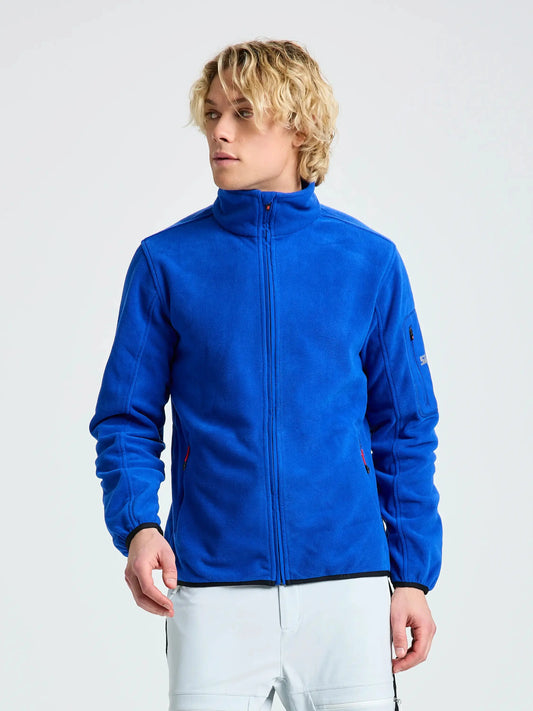 A person is standing against a plain light background, facing slightly to the side with hands relaxed at their waist, wearing the SLAM DECK FLEECE men’s zip-up jacket in OLYMPIC BLUE.