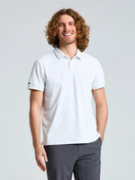 A person with curly, shoulder-length hair wears the SLAM TECH PIQUE POLO SS in OFF WHITE along with dark pants, standing and smiling against a plain light gray background.