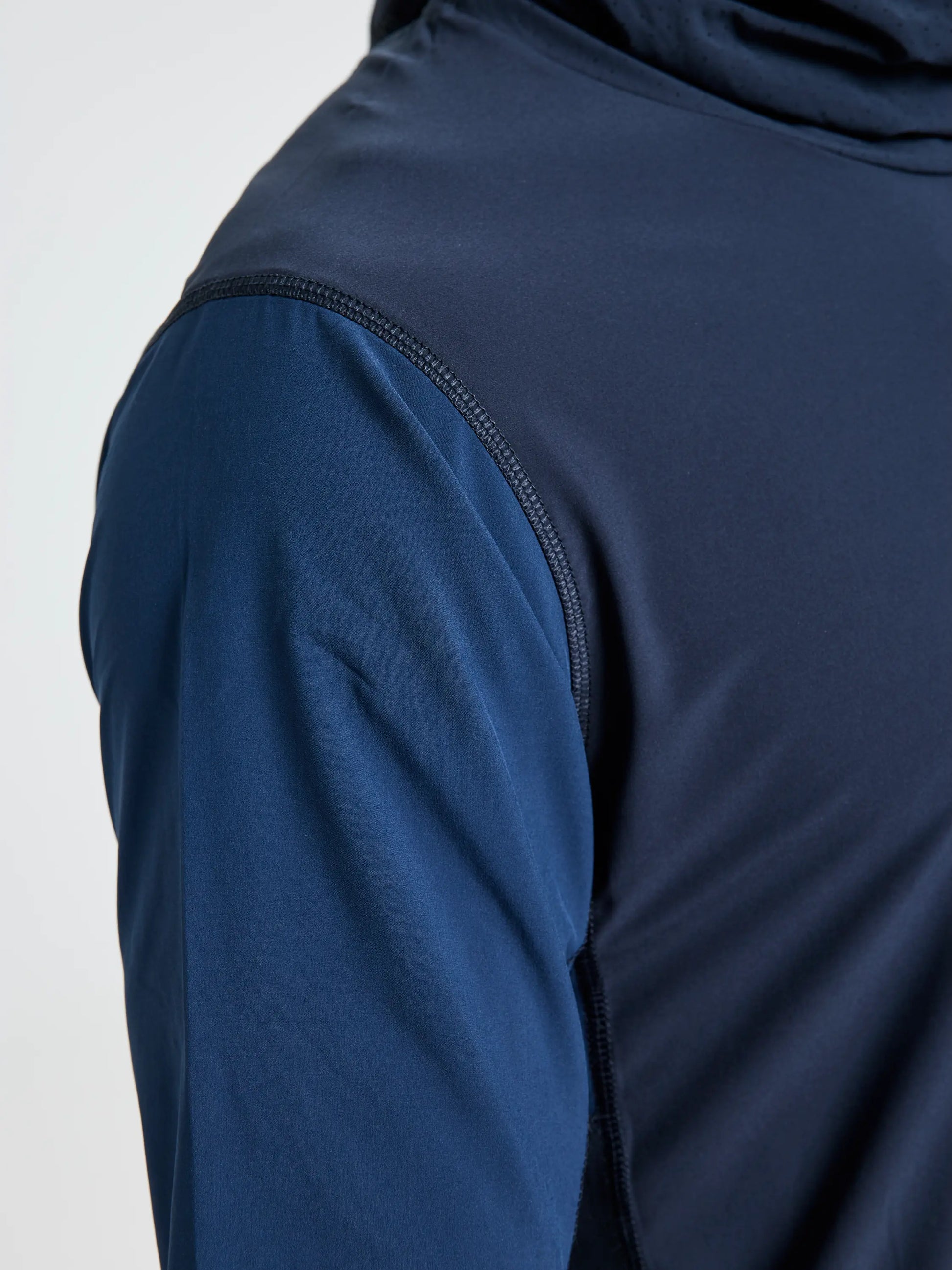 A close-up of a person wearing the SLAM OD TECH HOODED T-SHIRT in navy blue, highlighting the shoulder, upper arm, visible stitching, and smooth windproof fabric texture.