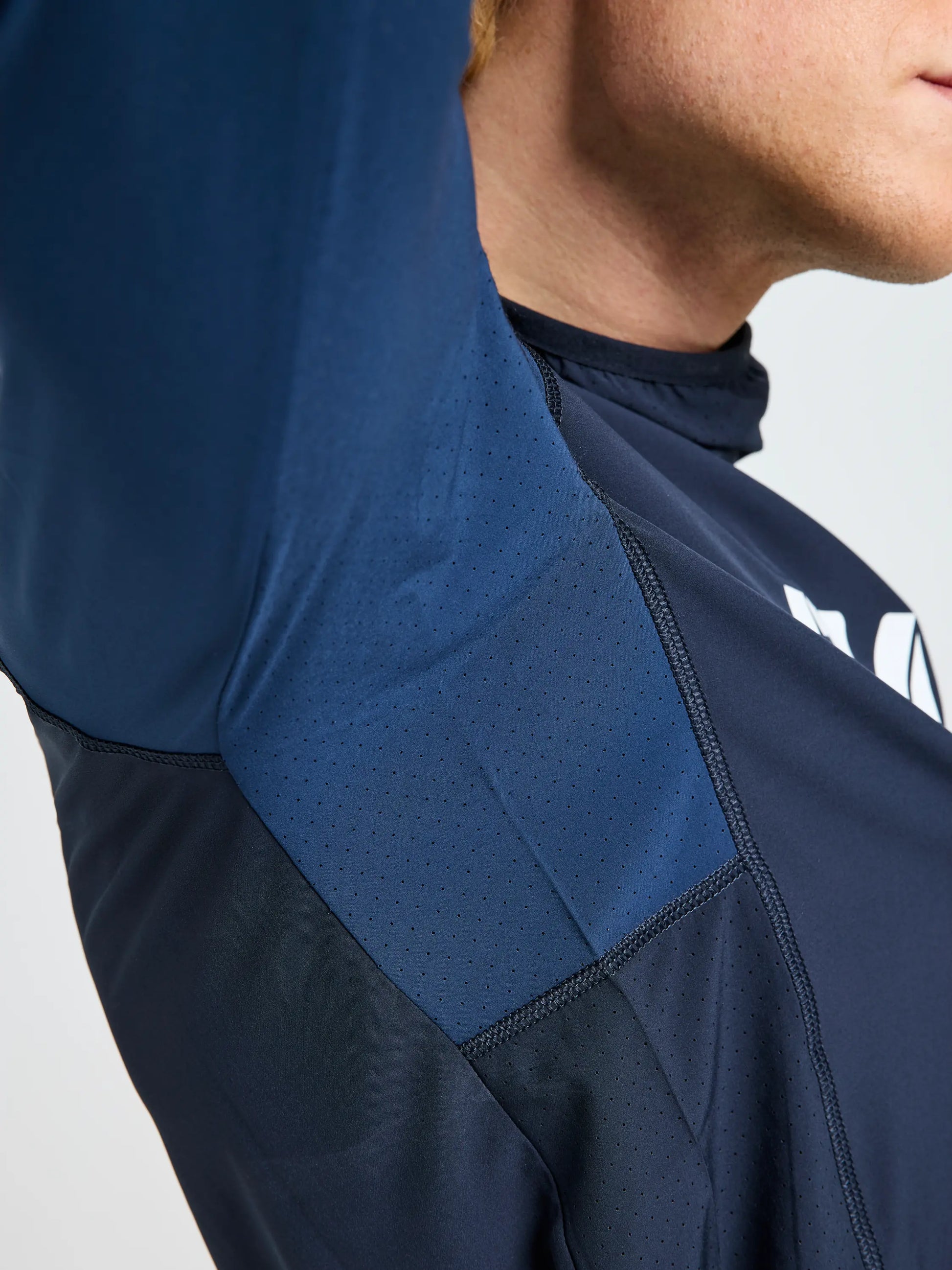 A close-up of a person in the SLAM OD TECH HOODED T-SHIRT, cropped to show the lower face, neck, and upper torso, highlights navy perforated underarm fabric as they raise their arm to reveal ventilation details.