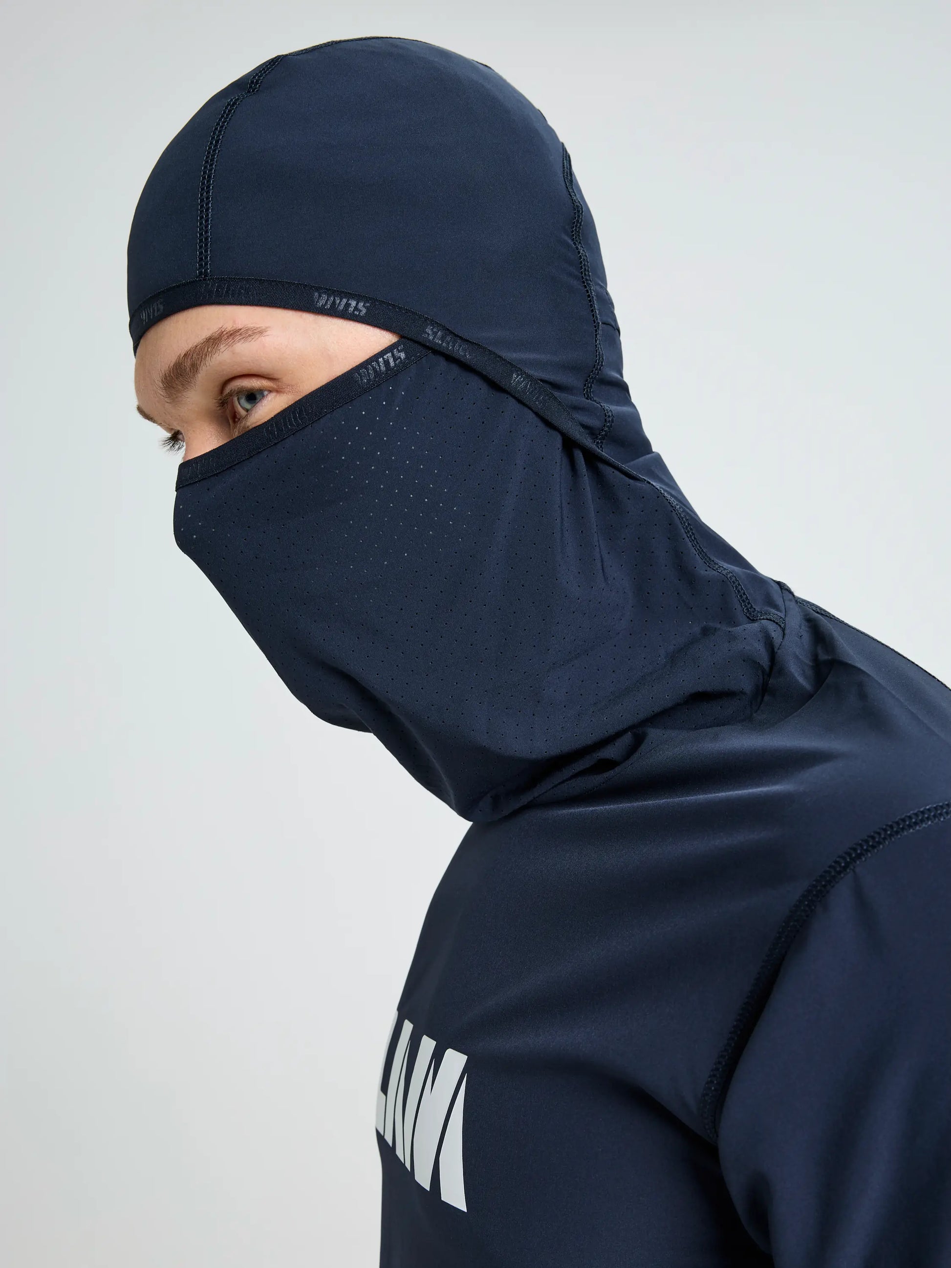 A person wearing the SLAM OD TECH HOODED T-SHIRT in navy blue, a windproof hooded garment covering the head, neck, and lower face with only the eyes and part of the forehead visible. It features small ventilation holes near the nose and mouth.