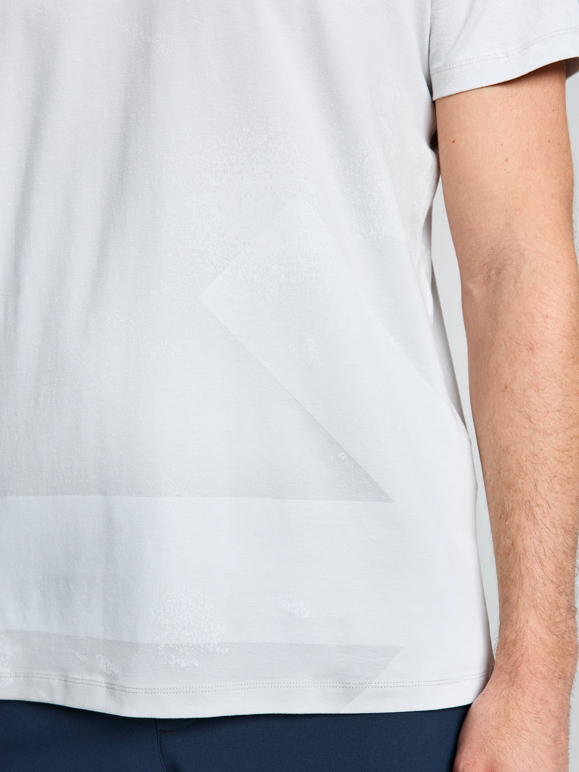 A person wearing the SLAM WIND MAP T-SHIRT in light gray and dark pants, shown from shoulders to hips with one arm visible on the right side.