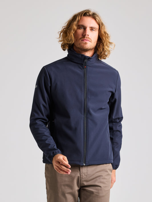 A person with wavy, shoulder-length hair is wearing a DARK NAVY ACTIVE WARM SOFTSHELL JACKET by SLAM and beige pants. They are standing against a plain white background.