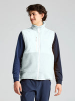 A person stands against a plain background wearing the SLAM ALTURA VEST in light blue over a navy long-sleeve shirt and navy pants, looking off to the side and smiling.