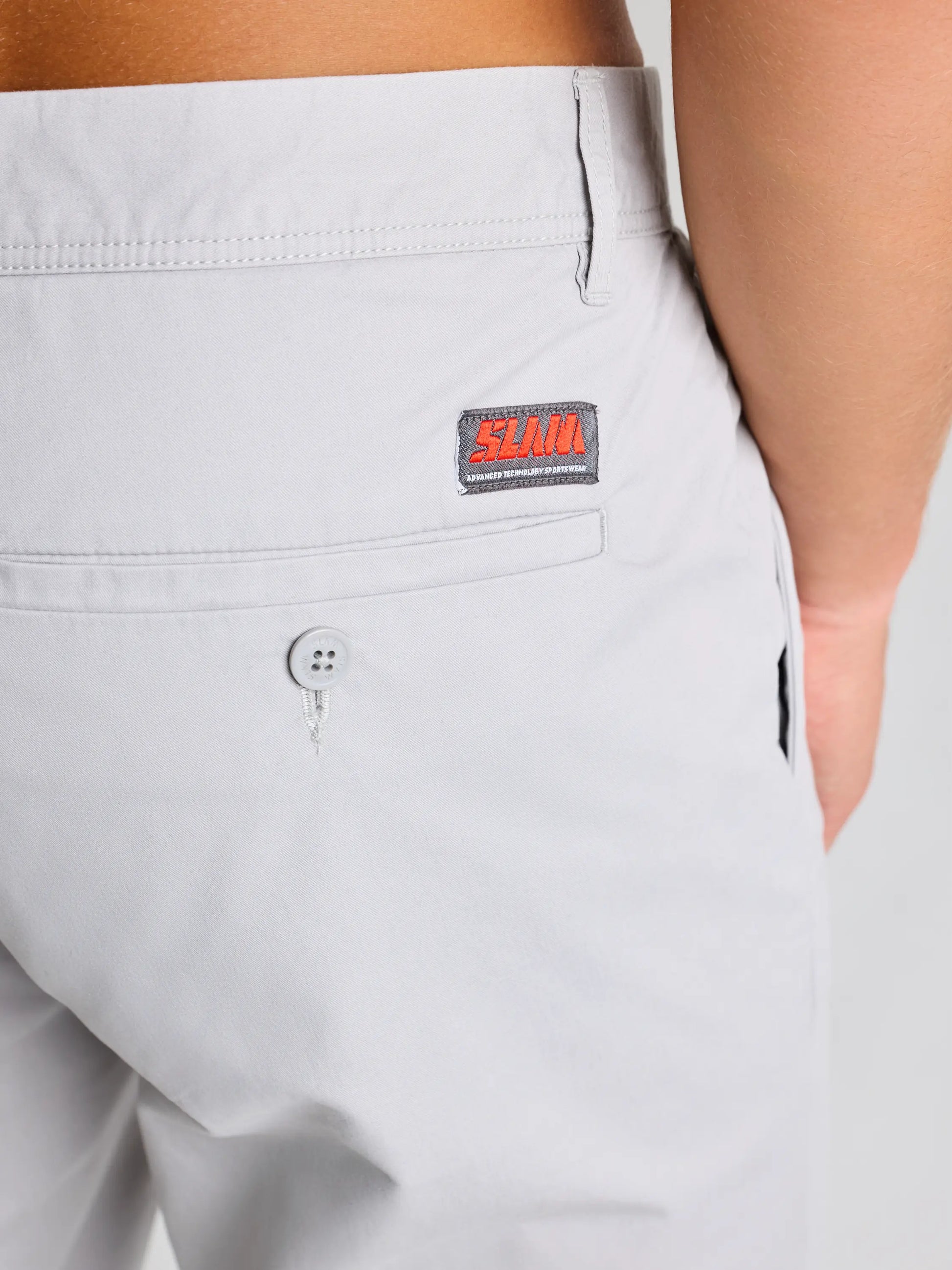 Close-up of a person in SLAM's DECK LGT CHINO SHORT: light gray twill cotton, side and buttoned back pockets, with a "SLIM" patch on the waistband—ideal for formal or casual wear.
