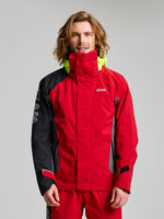 A man with long hair wears a SLAM PRO COASTAL JKT in red and black, featuring a high collar and neon yellow hood, as he faces the camera against a plain light grey background.