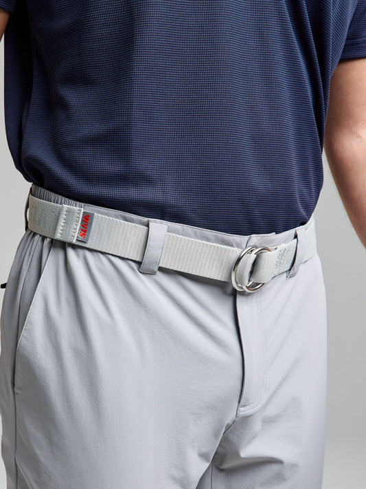 A person wearing a blue checkered shirt tucked into light gray pants, complemented by the SLAM LOGO BELT. The belt, featuring a jacquard logo and a silver buckle with a small red tag, draws attention to the waist and midsection.