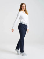 A person with long hair, dressed in a white long-sleeve shirt, navy blue technical trousers, and gray sneakers, walks forward in a studio with a plain white background while wearing the SLAM LOGO BELT 2.0.