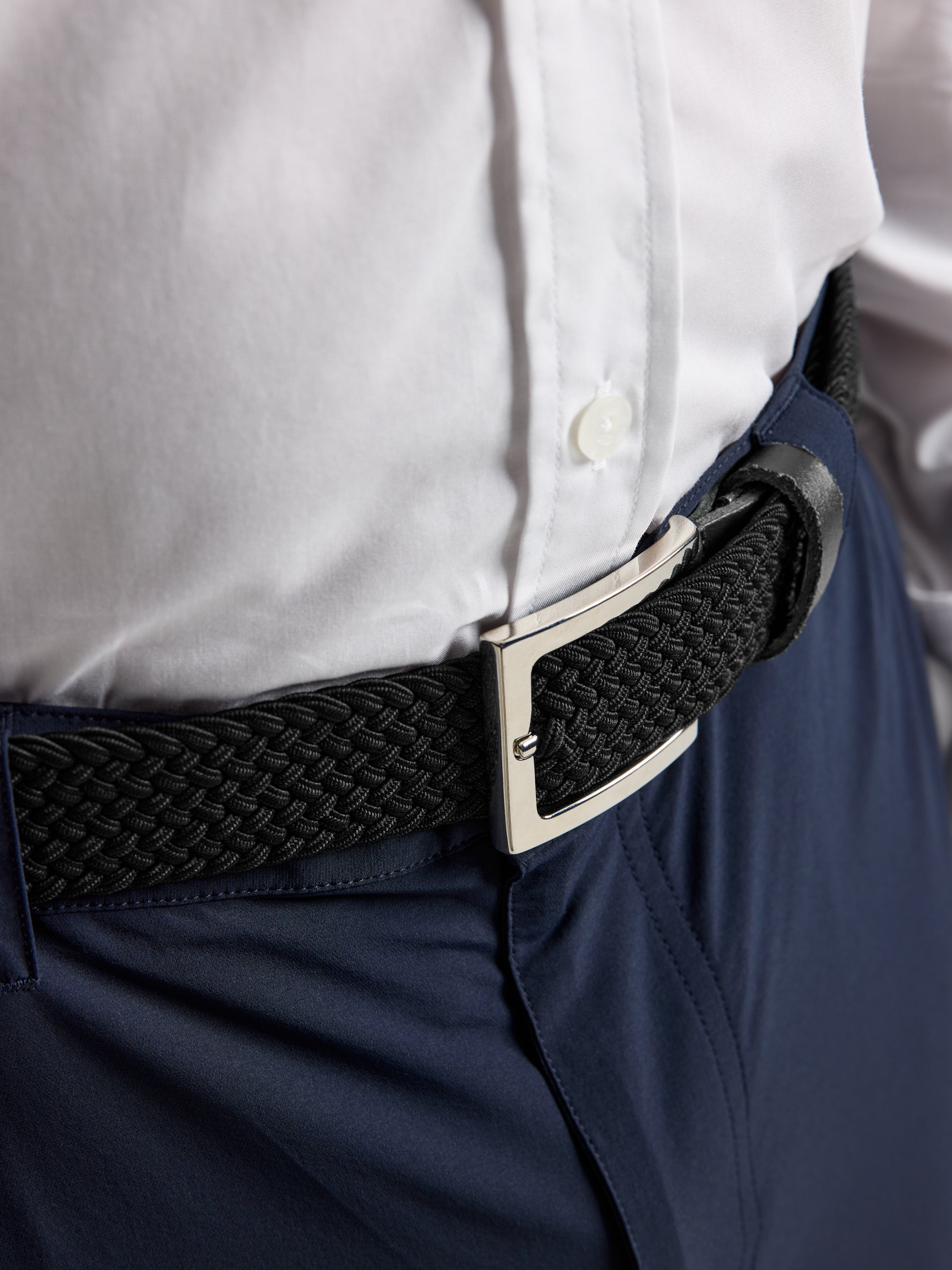 A close-up of a person wearing SLAM's DECK BELT in BLACK INK with a polished nickel buckle, styled with a white shirt and navy trousers for a refined nautical look.