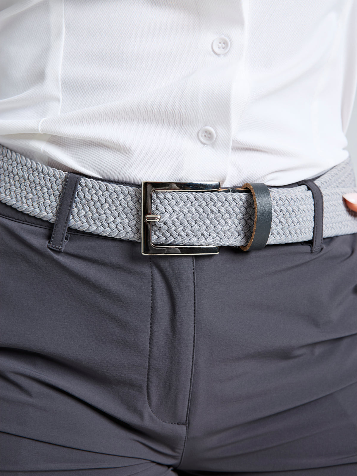 A grey woven elastic SLAM DECK BELT with a nickel buckle worn over dark trousers.