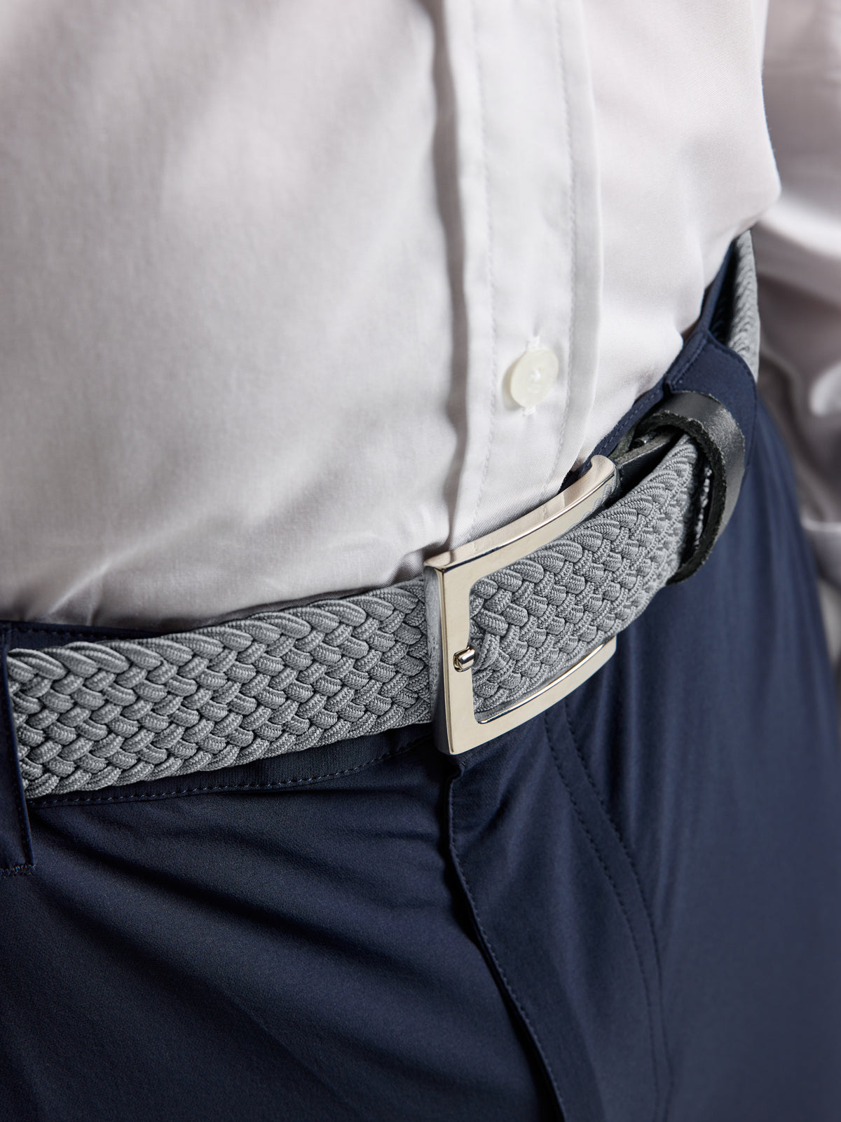 A grey woven elastic SLAM DECK BELT with a rectangular silver buckle worn over navy trousers and a white shirt.