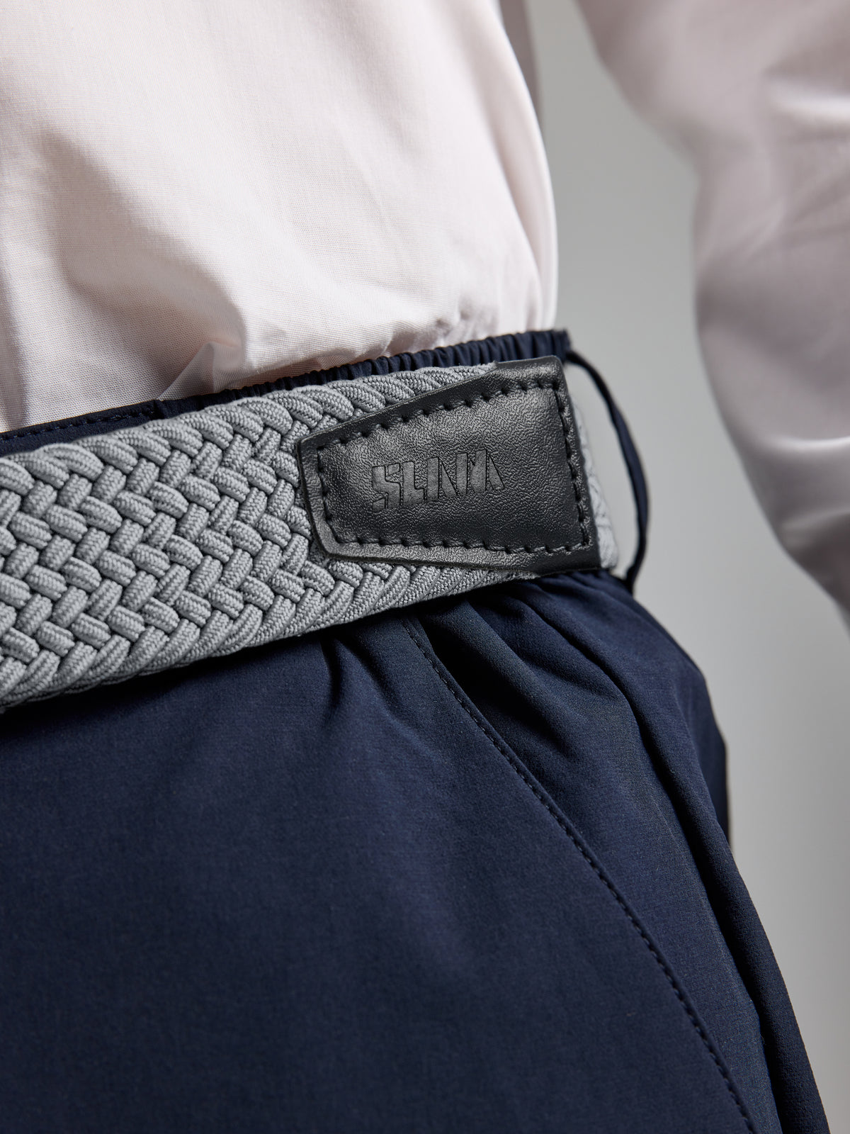 A grey woven elastic SLAM DECK BELT with a nickel buckle worn with navy trousers and a white shirt.