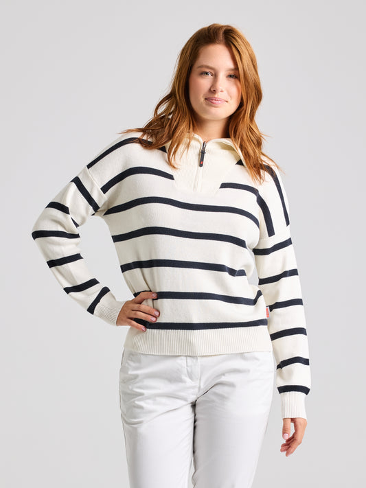 A woman dressed in the WOMAN JUMPER LLYR CL by SLAM, made from a cotton/merino wool blend with a stylish white and navy striped design, stands elegantly against a plain background. The chic sweater features a zip-up collar, and her hand rests casually on her hip.