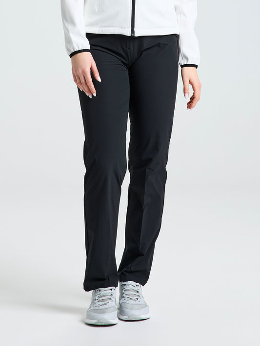 A person facing forward wears SLAM's WS TECH CHINO PANT in black, a white jacket, and gray athletic shoes. The image is cropped at the shoulders.