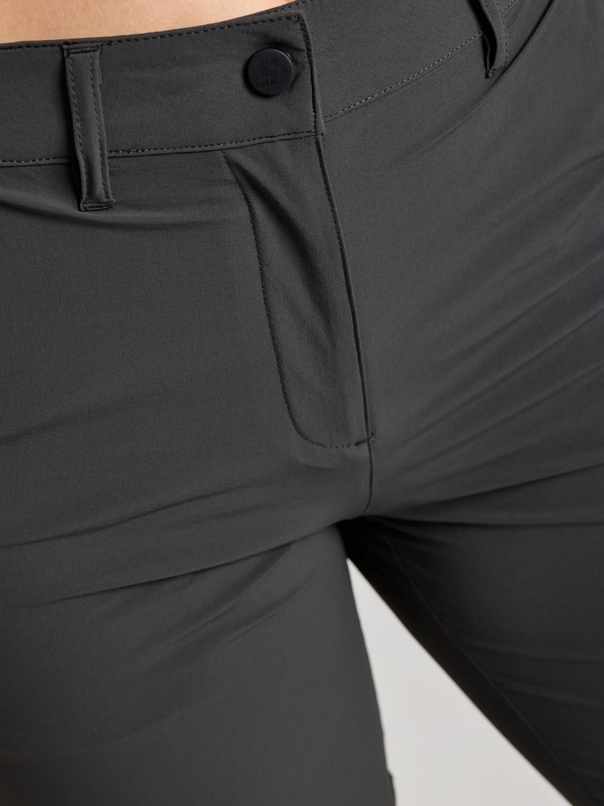 Close-up of a person wearing SLAM WS TECH CHINO PANT in dark gray, showcasing the waistband, button, zipper area, and upper thigh details.