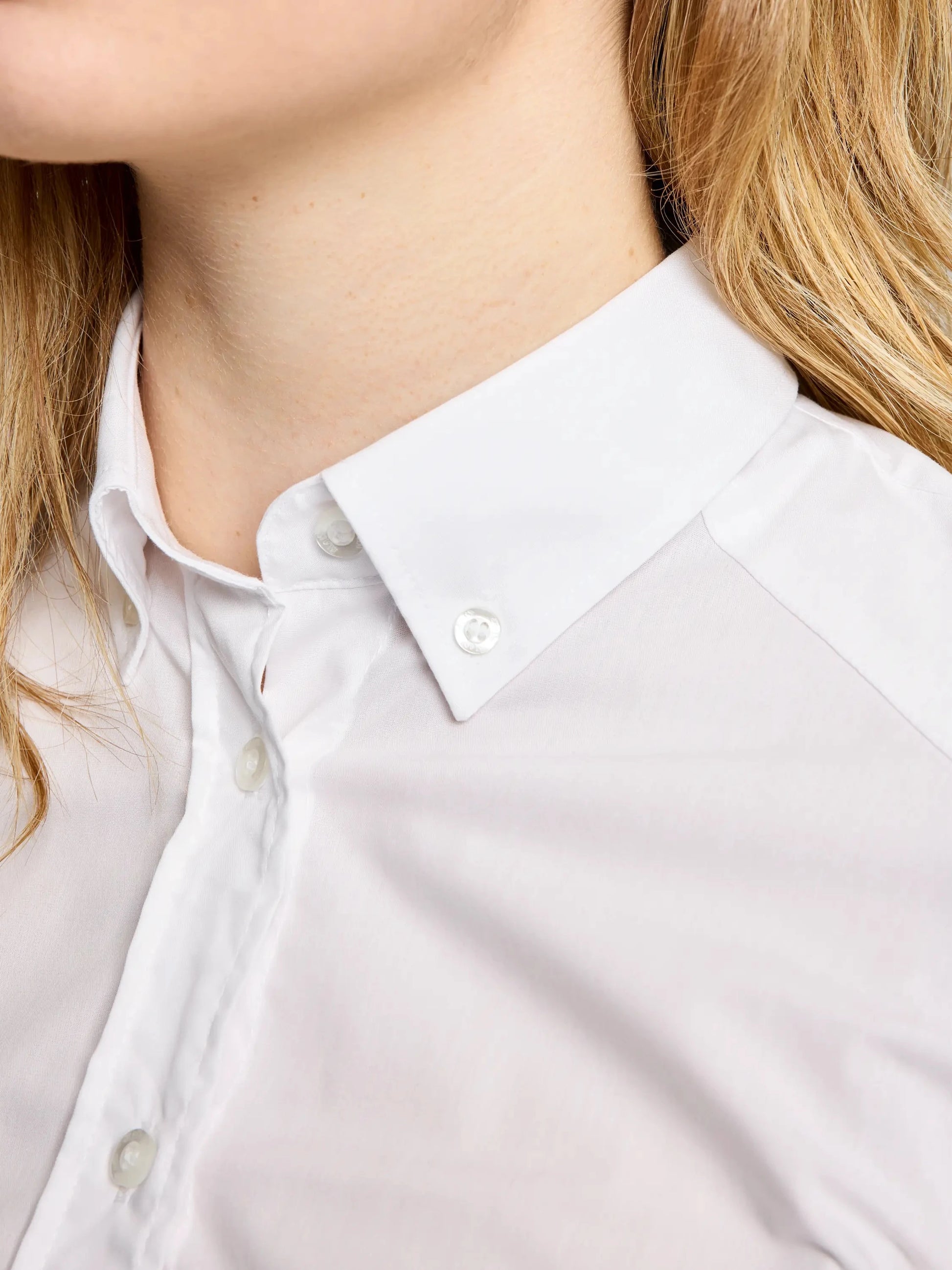 Close-up of a person wearing the SLAM DECK WS NO IRON SHIRT, a pure cotton button-up with a classic cut and collared neckline, buttoned to the top. The person’s blonde hair is partially visible against a neutral, out-of-focus background.