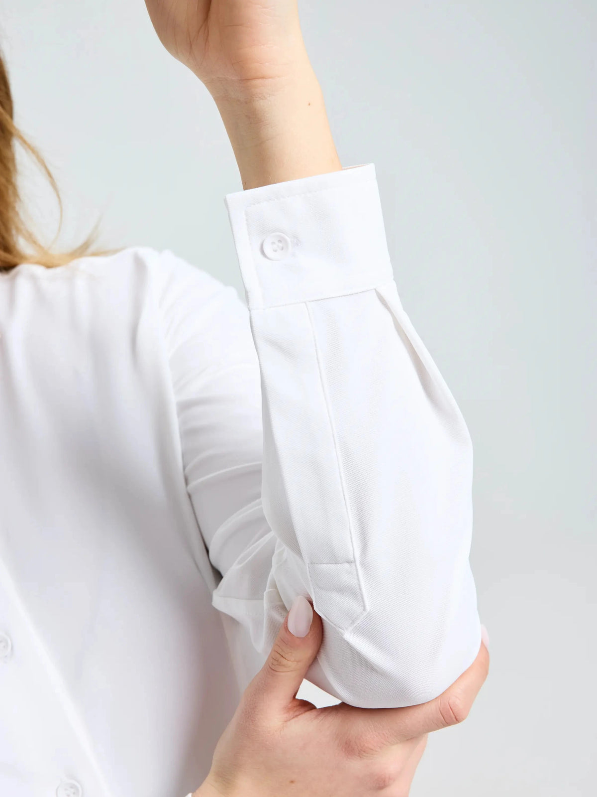 A person is shown rolling up one sleeve of the SLAM WS TECH PIQUE SHIRT LS in white, gripping the fabric with the cuff visible. Featuring UPF 50+ sun protection, this long-sleeve technical shirt stands out against a plain, light-colored background.