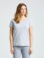 A woman with long, light brown hair stands against a plain background, wearing the SLAM WS TECH PIQUE T-SHIRT in light gray and matching pants, looking slightly left with a neutral expression.