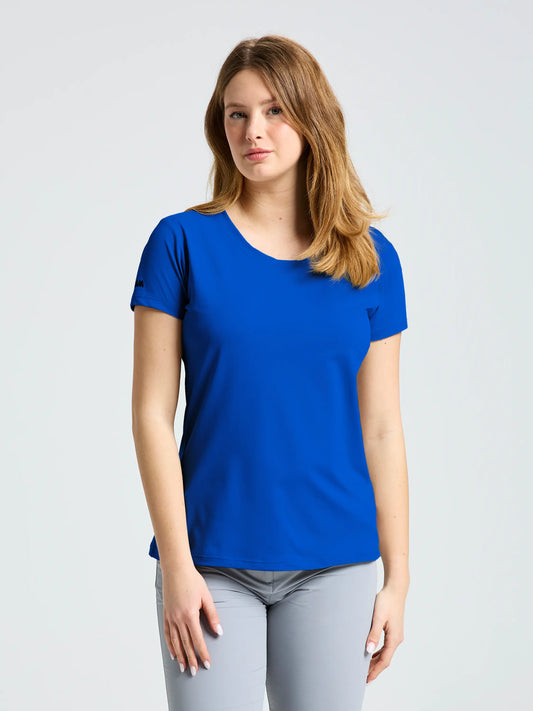 A person with long, light brown hair stands against a plain background, facing forward and wearing the SLAM WS TECH PIQUE T-SHIRT in bright blue with light gray pants, arms relaxed at their sides.