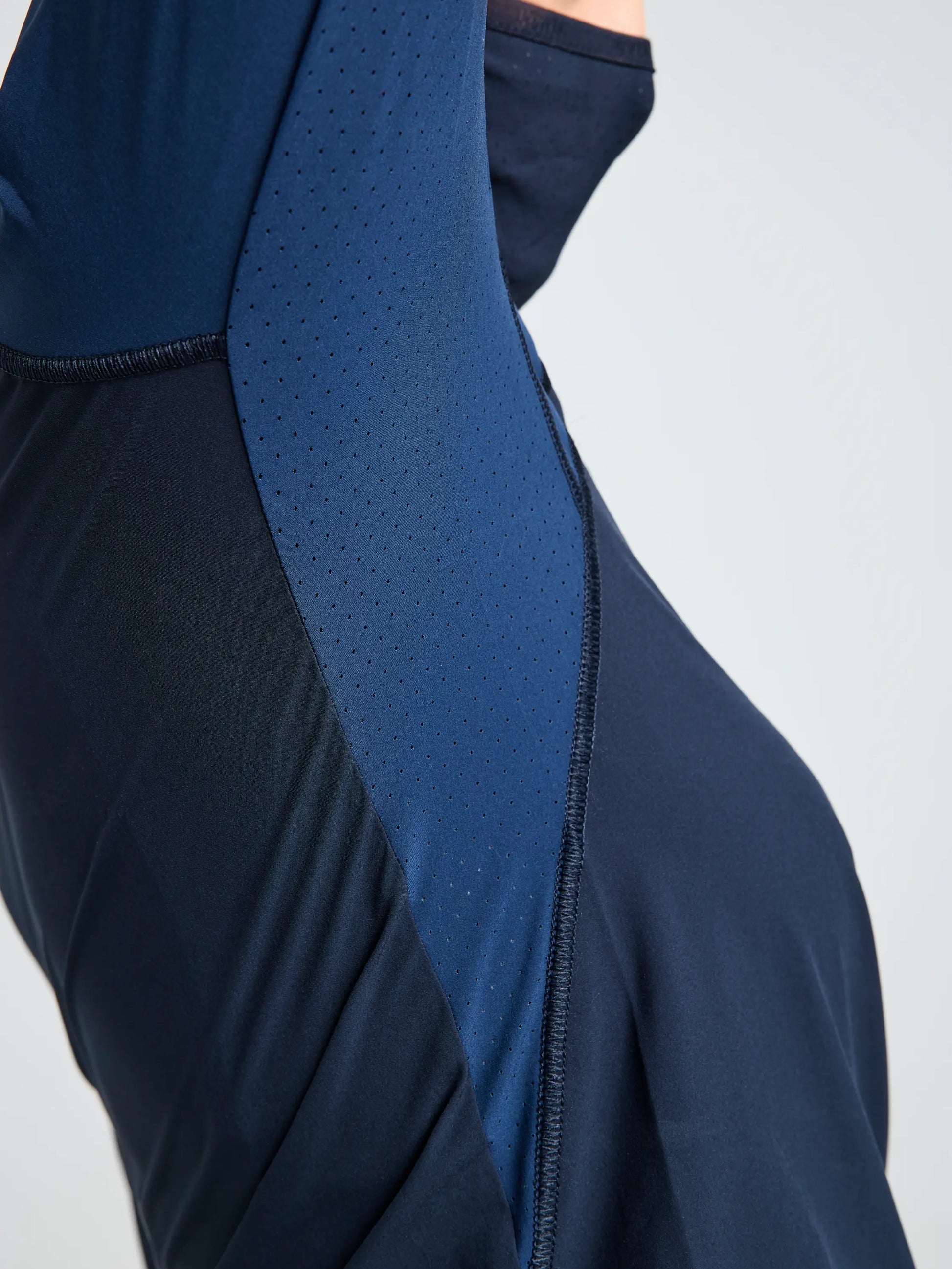 Close-up of a person wearing the SLAM OD WS TECH HOODED T-SHIRT in navy blue, featuring recycled stretch fabric with perforated, breathable underarm panels and visible stitching.