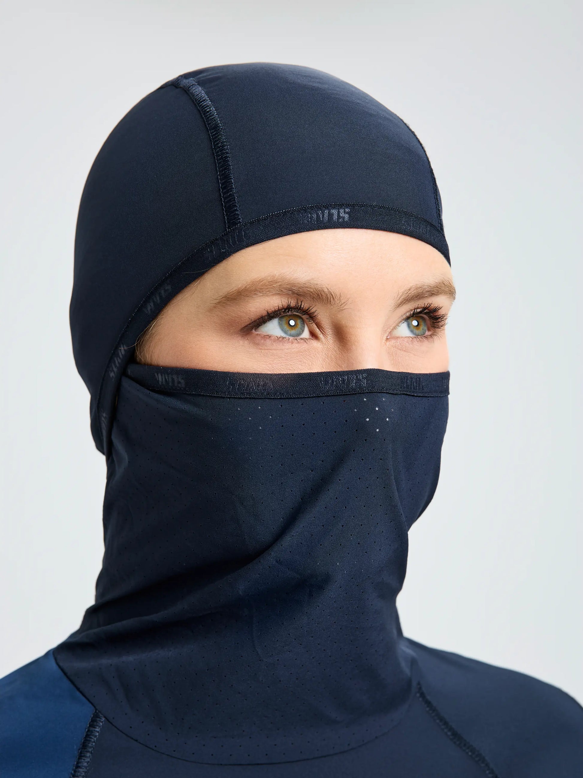A person wears the SLAM OD WS TECH HOODED T-SHIRT in dark navy blue with a matching perforated face covering, exposing only their eyes, eyebrows, and part of the forehead, set against a plain light background.