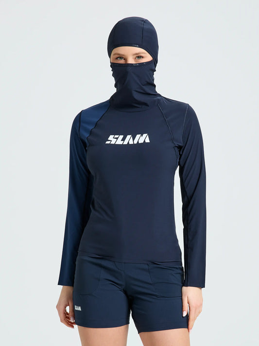 A person wears the SLAM OD WS TECH HOODED T-SHIRT in navy blue, made from recycled stretch fabric, paired with shorts and a swim cap with face covering. "SLAM" appears in white on the chest. The background is plain and light-colored.