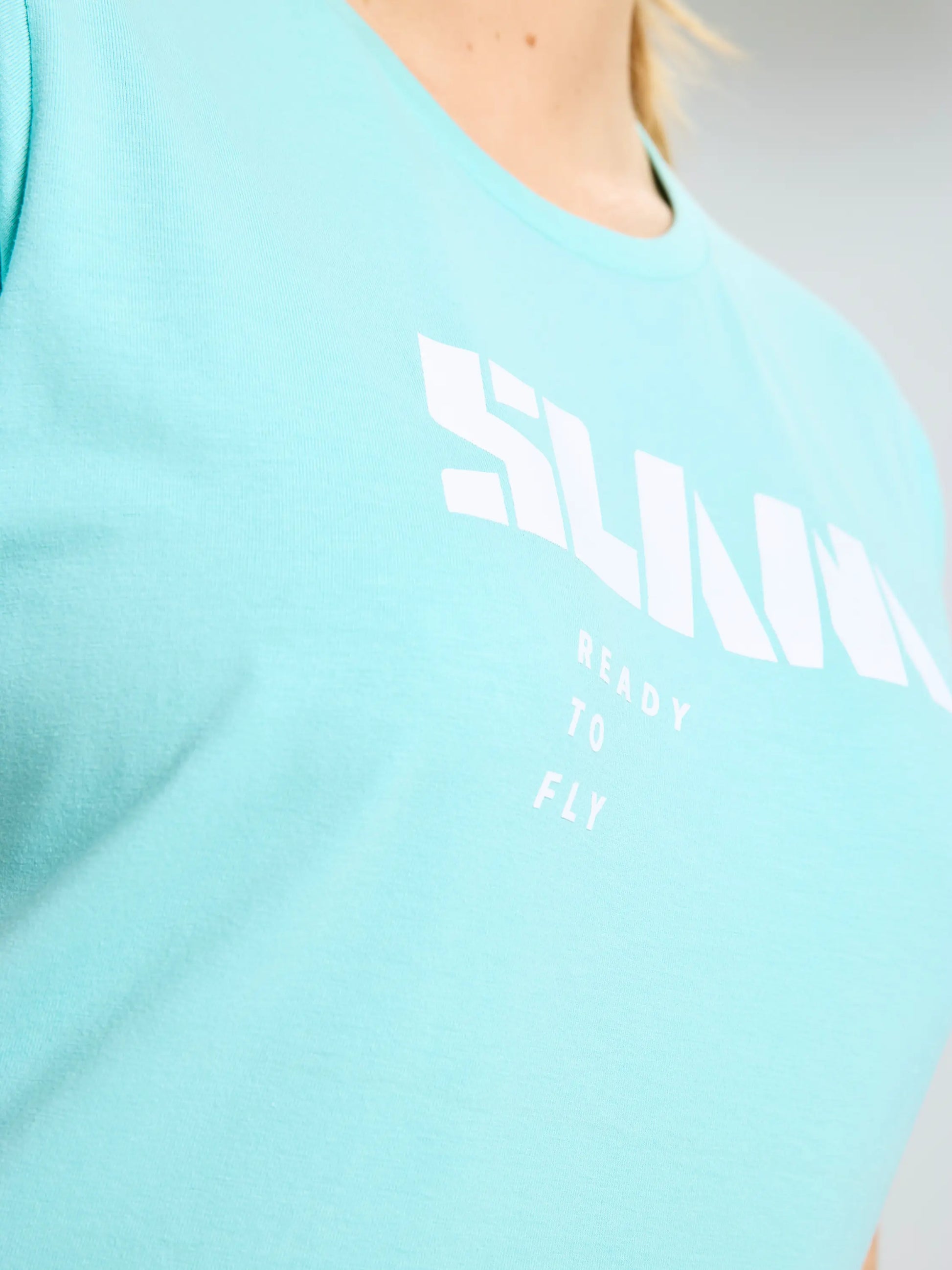 Close-up of a person wearing the SLAM GRAPHIC WS T-SHIRT SS in light blue, featuring “SLAM” in white block letters and “READY TO FLY” underneath in smaller white print.