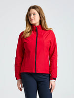 A person with long light brown hair wears the SLAM WS SAILING JACKET in REAL RED and dark pants, standing against a plain light background and looking slightly to the side.
