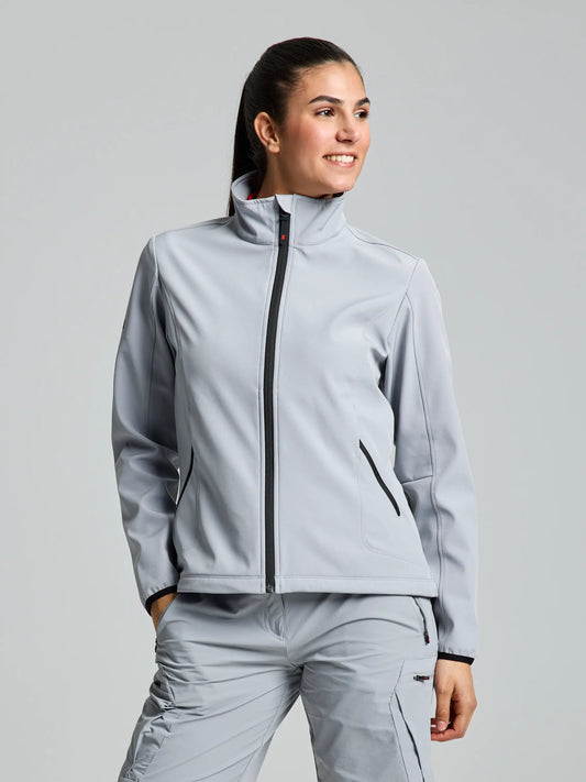 Dressed in an aluminium-colored ACTIVE WOMAN SOFTSHELL JACKET by SLAM, paired with matching pants, a person stands against a simple background. The windproof jacket features black zippers, and the person has their hair tied back, wearing a slight smile while looking off to the side.