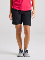 A person in a red shirt and SLAM WS TECH CHINO SHORT in BLACK INK, with gray athletic shoes, stands against a plain light background. Their arms are at their sides and their face is not visible.