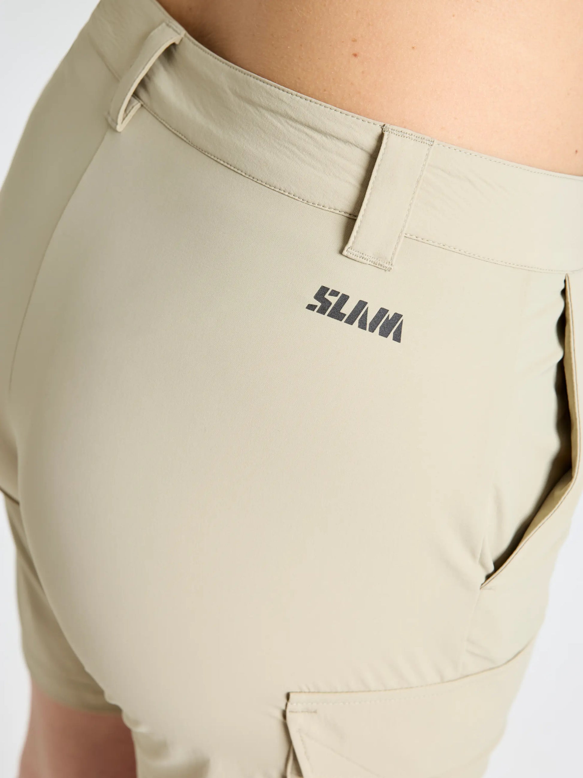Close-up of the back and side of a person wearing SLAM QD WS CARGO SHORT—light beige women's microfibre shorts featuring a black logo near the waistband, side pocket, and quick-drying fabric for comfort.