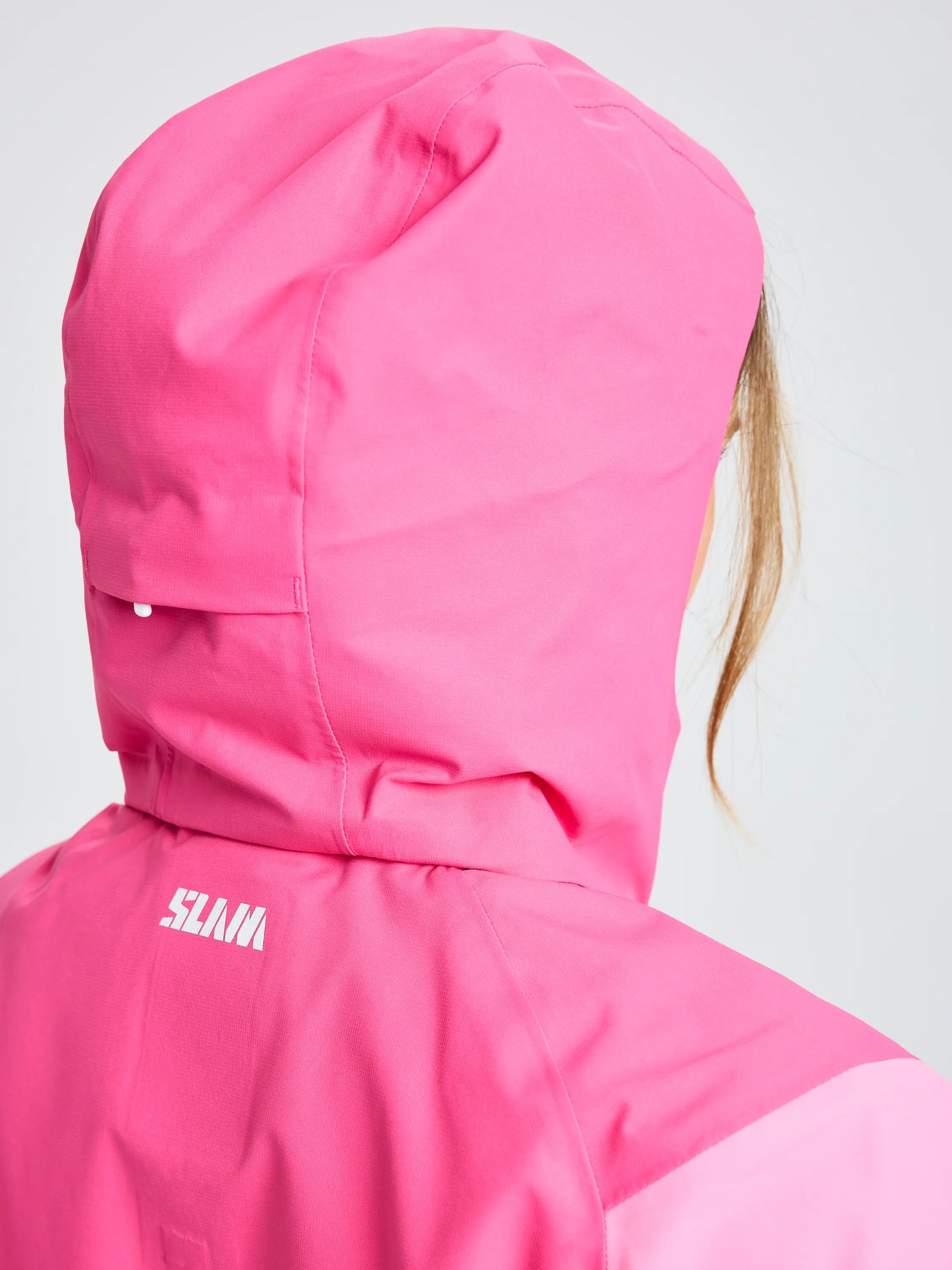 A person is seen from the back wearing a bright pink SLAM OD WS HOODED JACKET, featuring a white logo near the shoulder and only part of their hair visible.