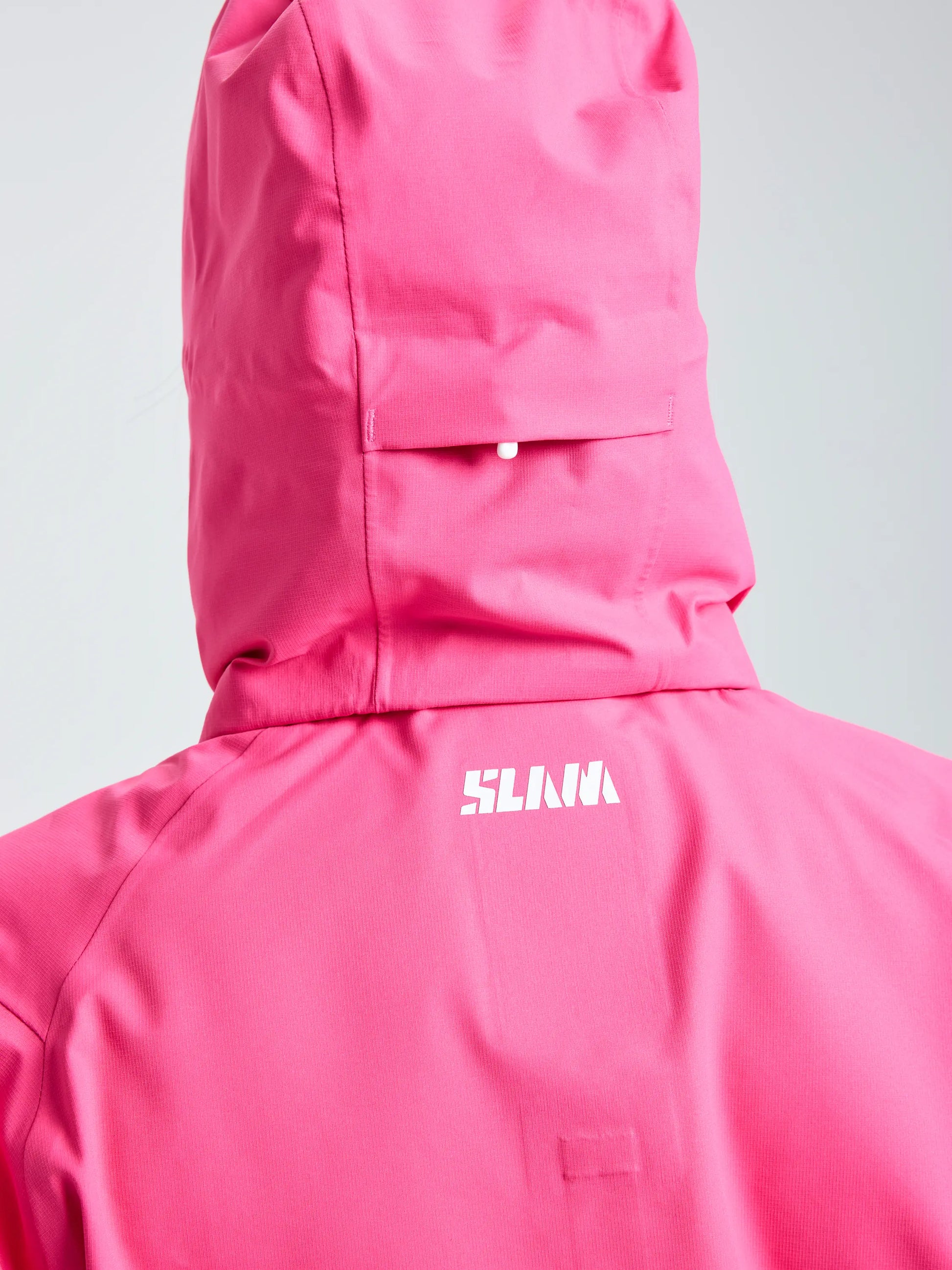 A close-up of the back of a person wearing the bright pink SLAM OD WS HOODED JACKET, featuring the white SLAM logo printed below the hood. The background is plain and light-colored.
