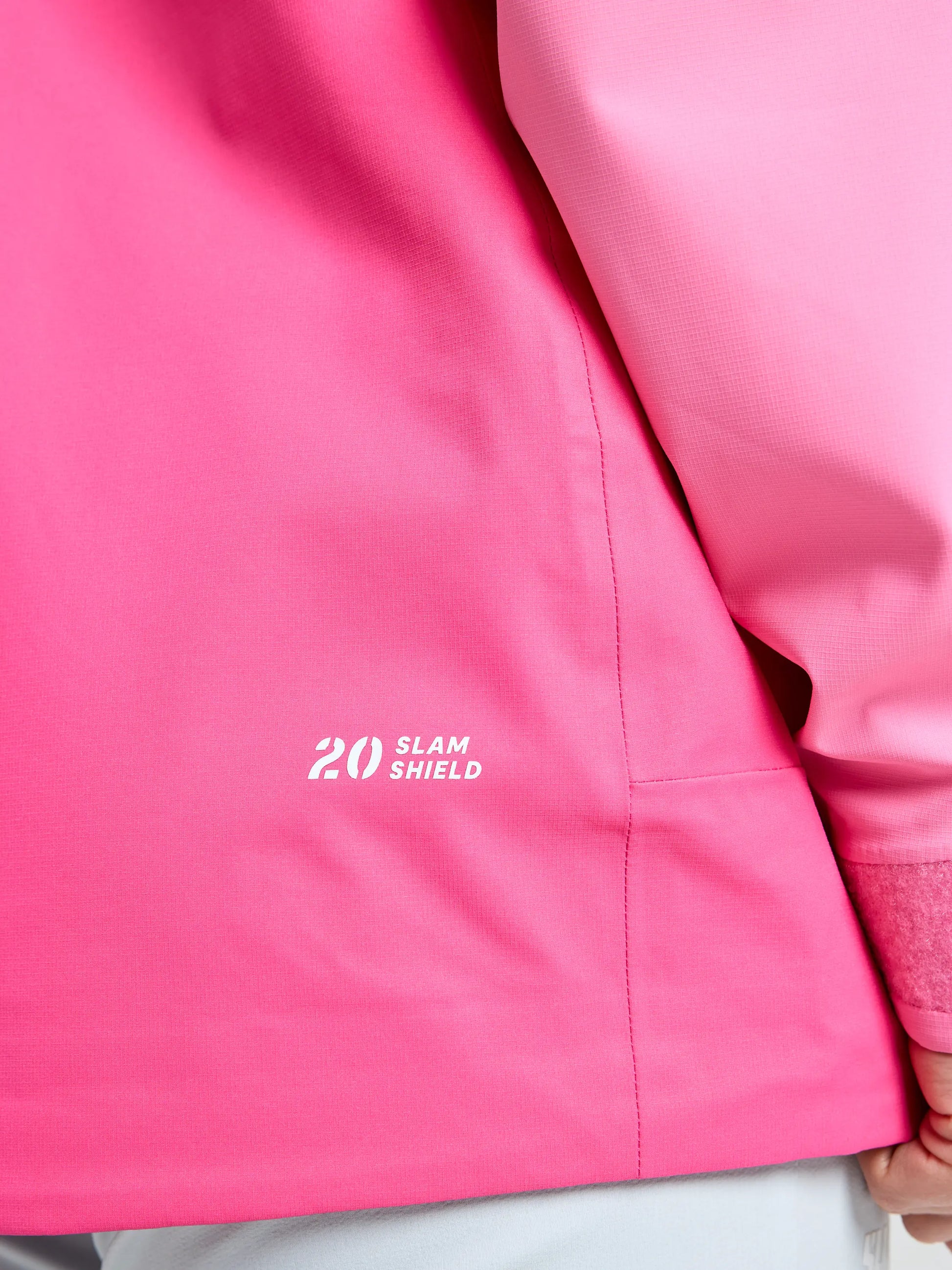 Close-up of the SLAM OD WS HOODED JACKET in bright pink, showing "20 SLAM SHIELD" in white on the side. This waterproof, breathable women's sailing jacket is pictured with a partially visible hand and a blurred background.