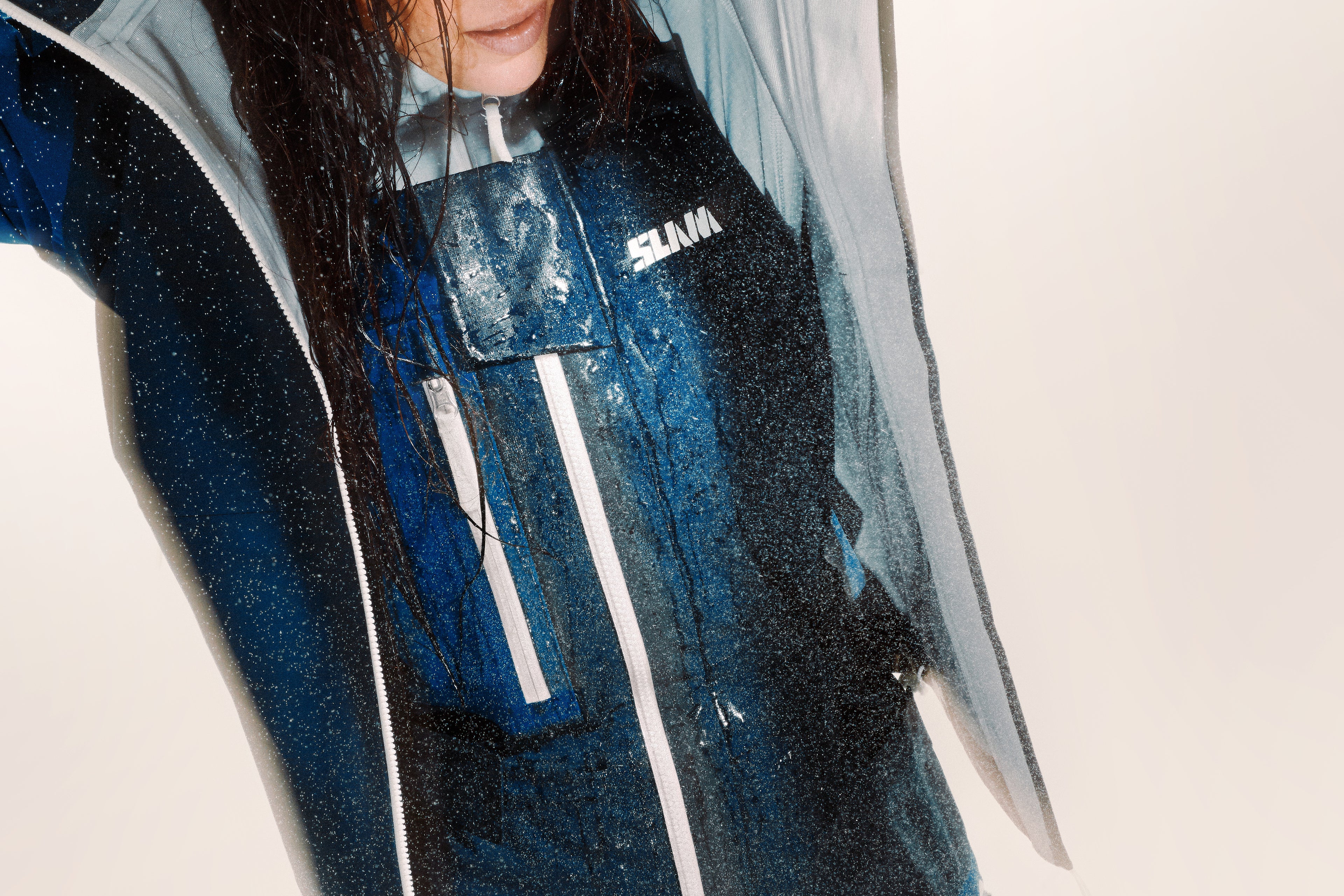 Woman with wet hair wearing a blue waterproof long john and a blue waterproof hooded jacket