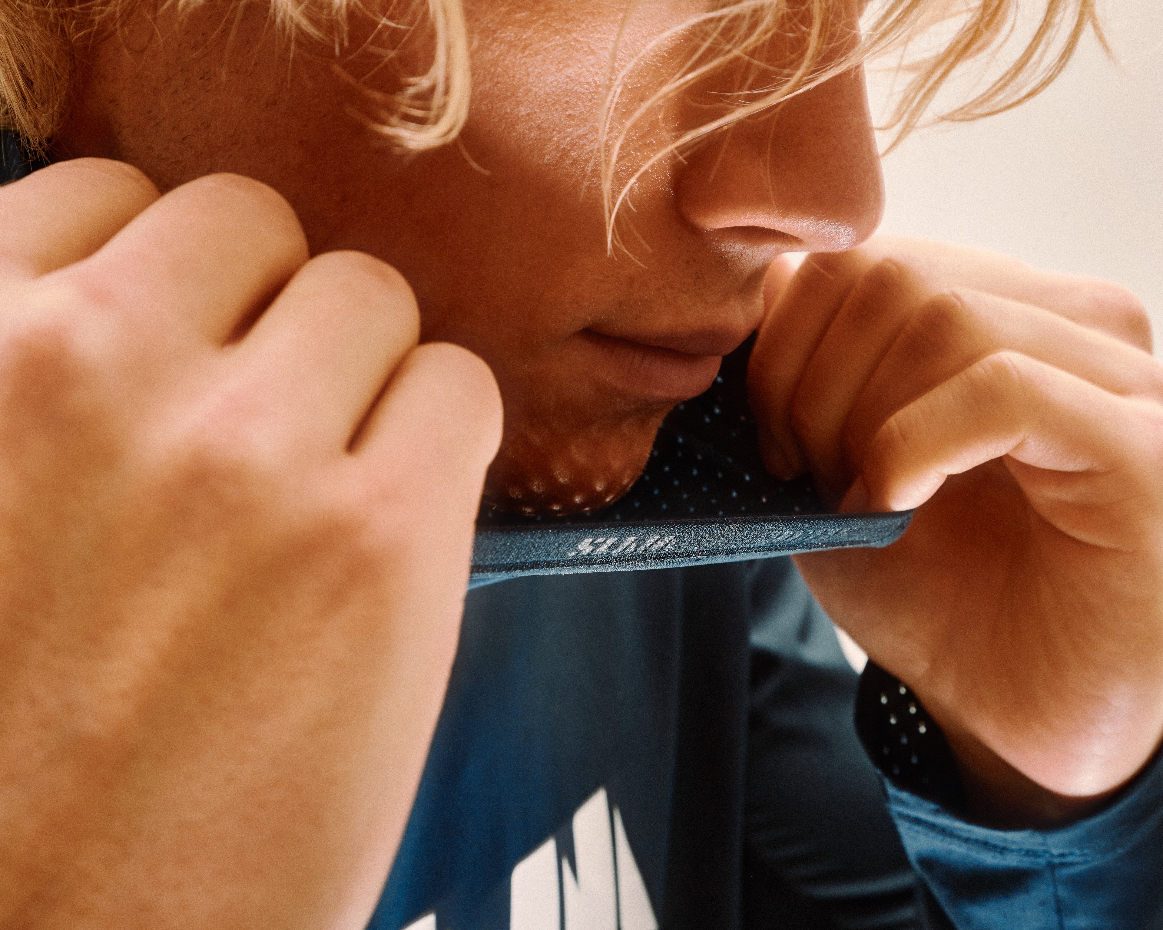 Close-up shot of a blonde man wearing a blue hooded t-shirt with a breathable neckbuff
