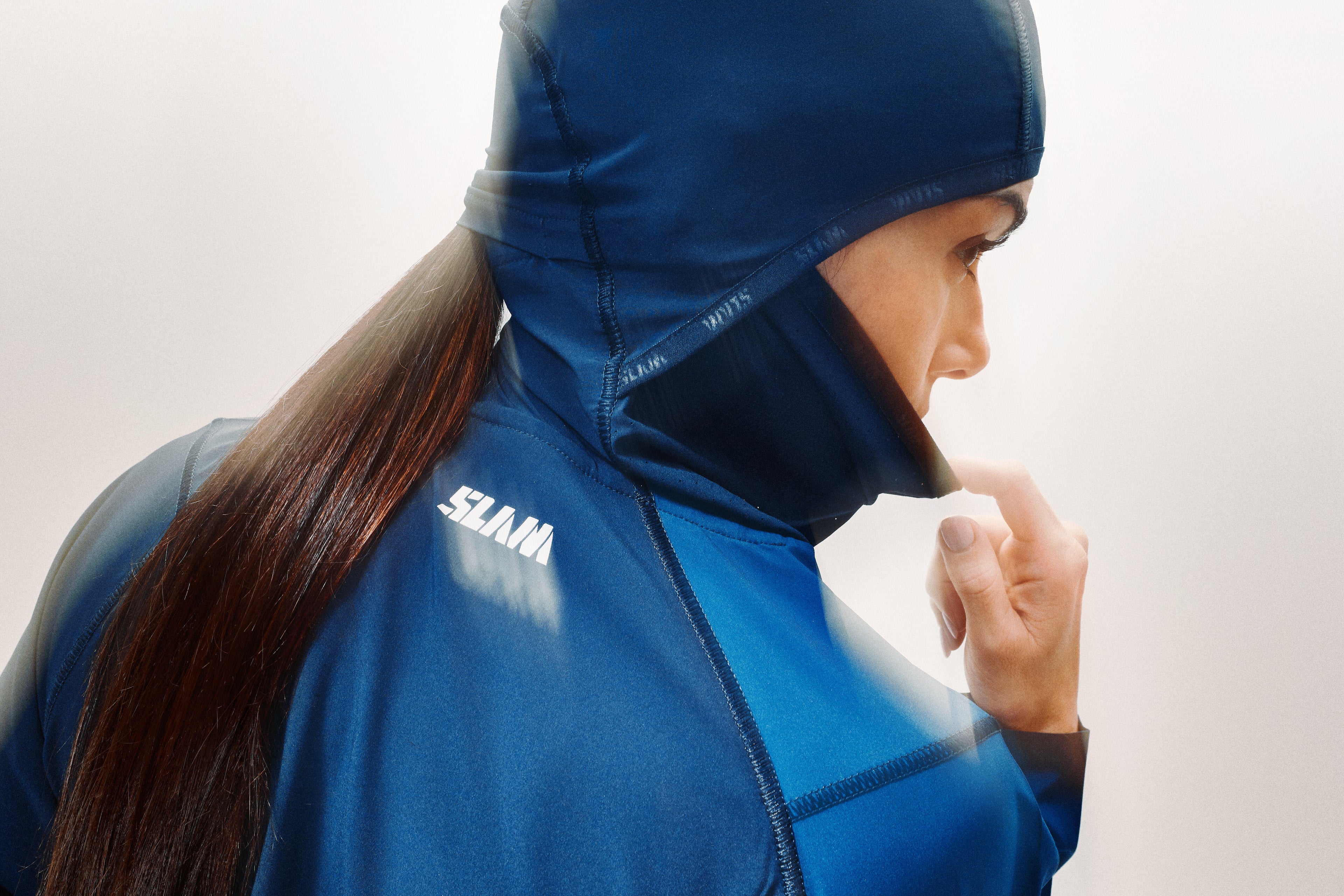 Donna indossa una maglia blu con cappuccio e scaldacollo tre in uno, con tanto di buco per far passare la coda sulla nuca