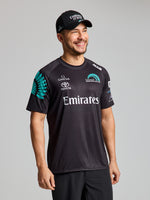 A man in a SLAM ETNZ SUNBLOCK SS shirt, ETNZ BLACK, with UV protection and Emirates, Omega, and Toyota logos, smiles in an 