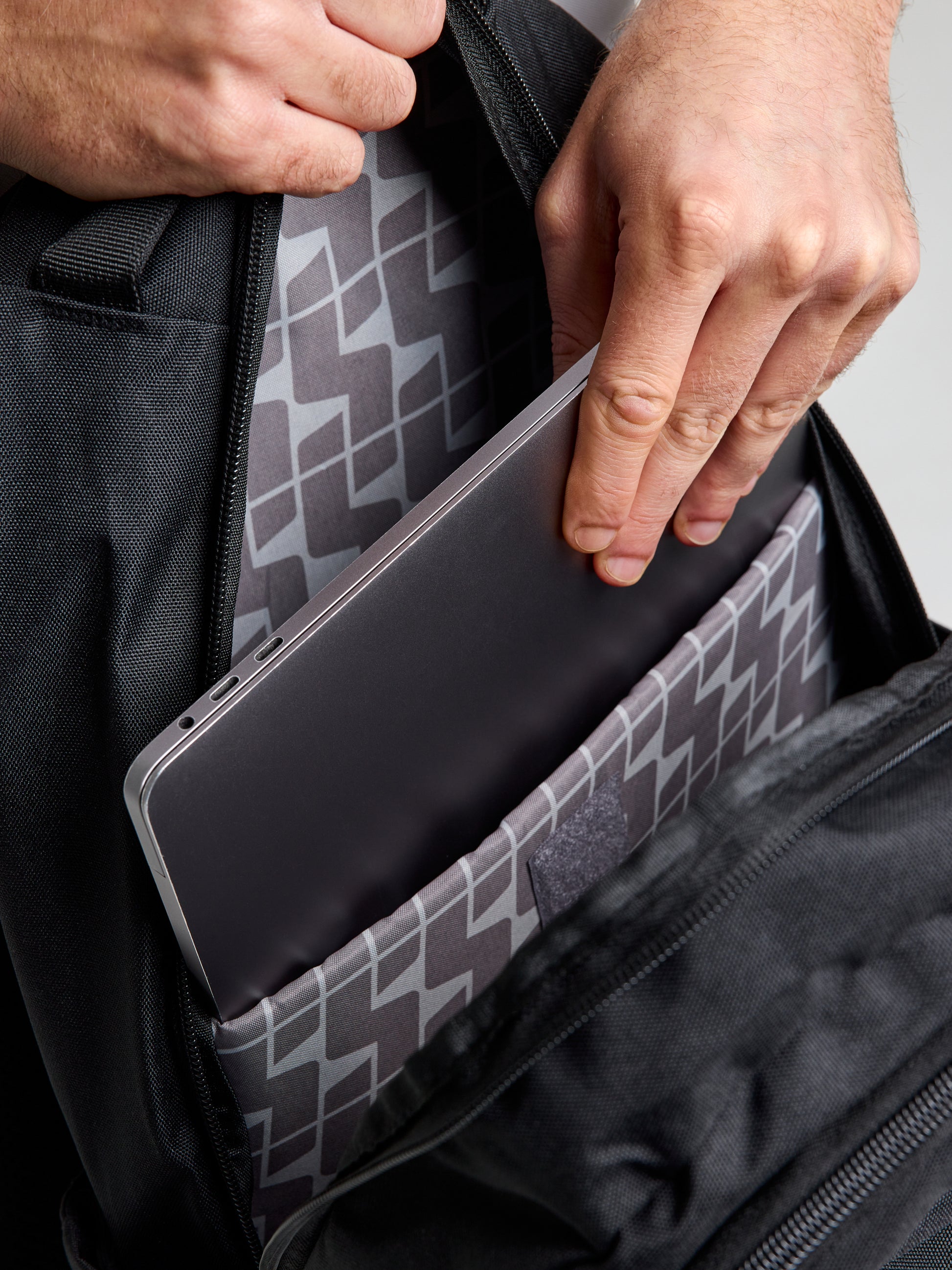 A person puts a gray laptop into the padded compartment of a SLAM ETNZ BACKPACK, featuring a geometric patterned lining inspired by Emirates Team New Zealand and the thrill of the America’s Cup.