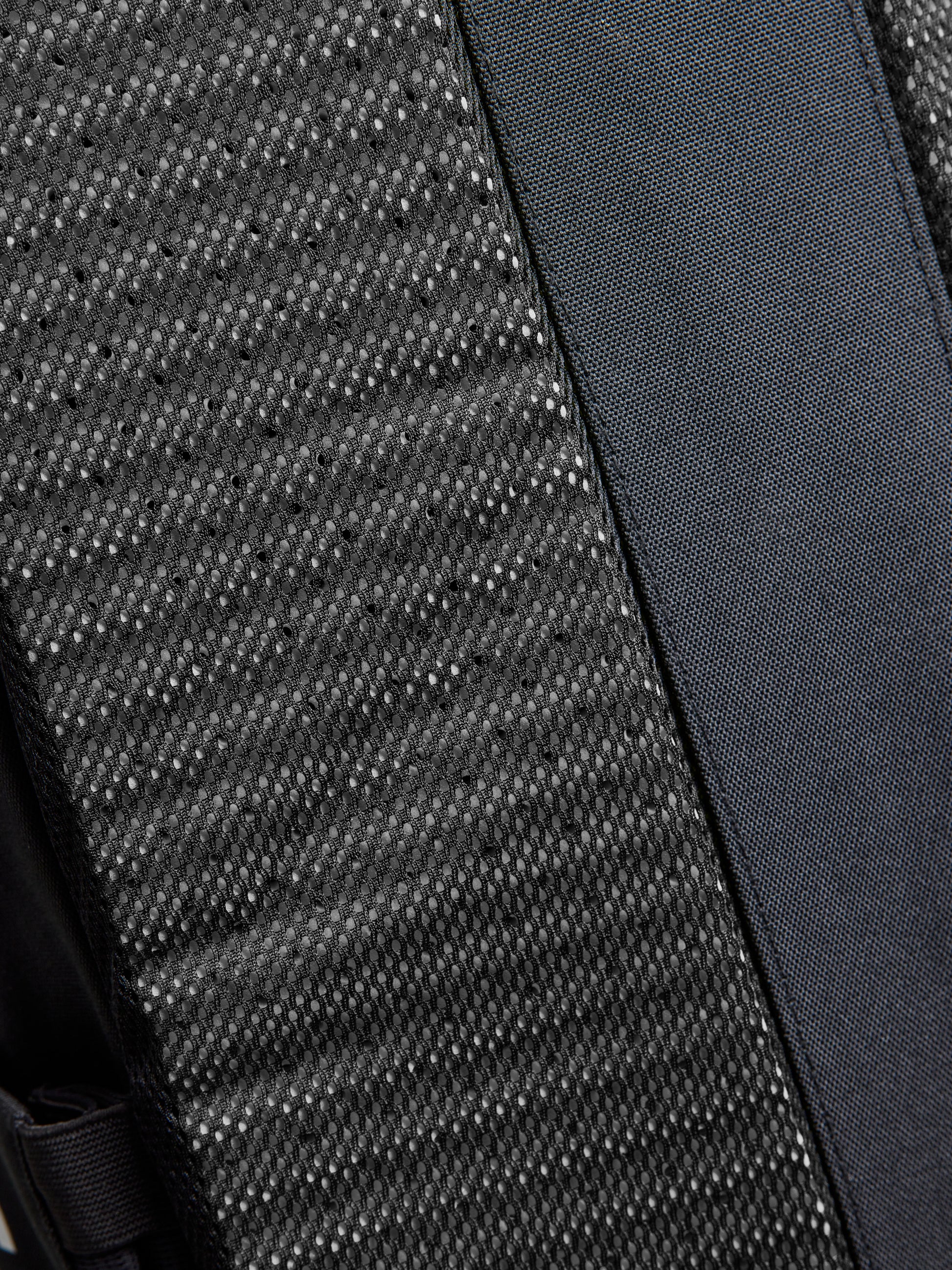 Close-up of a black textured fabric with a woven pattern next to a smooth, tightly woven strap, both part of the SLAM ETNZ BACKPACK inspired by Emirates Team New Zealand and the America's Cup.