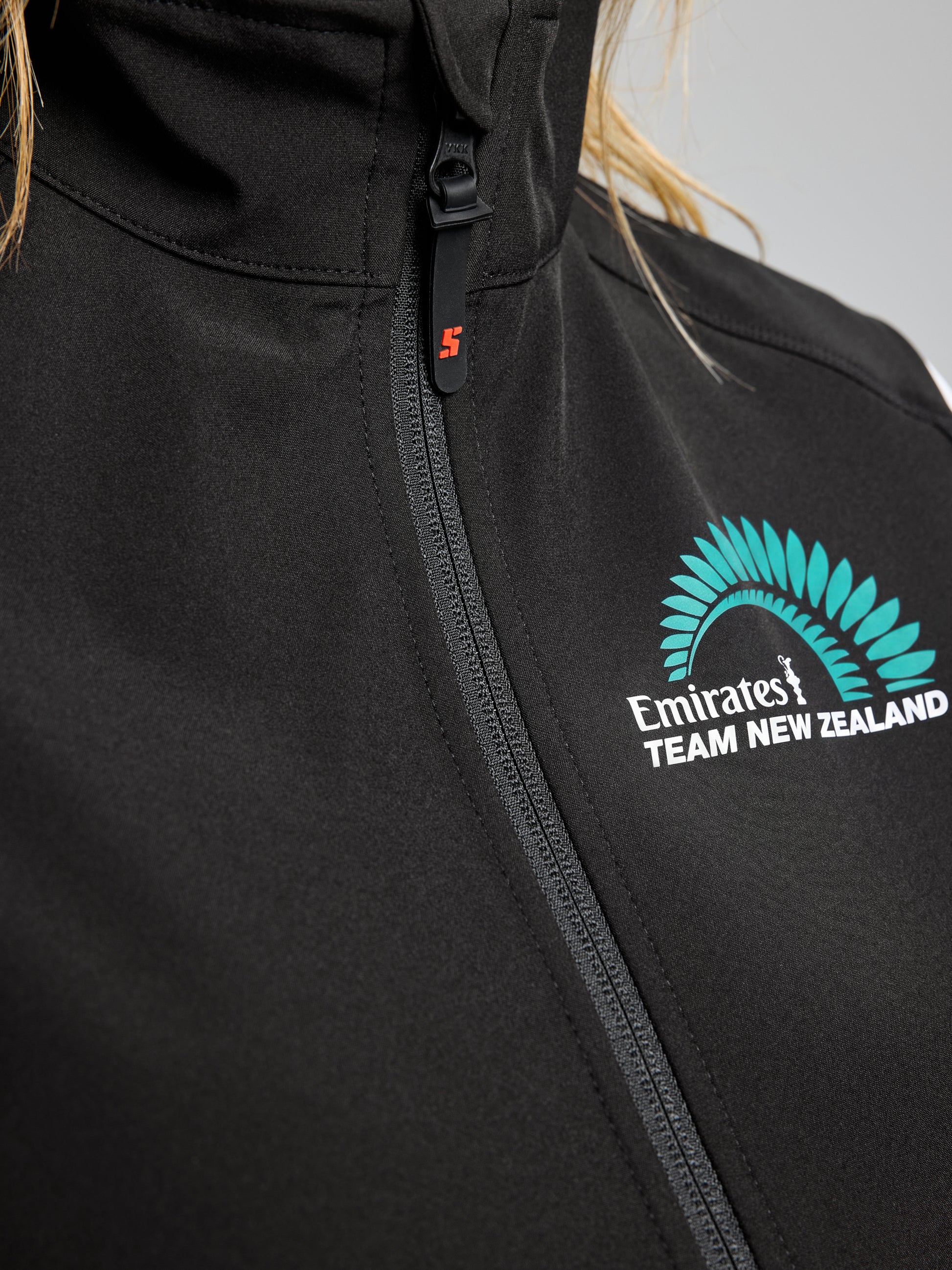 Close-up of the SLAM ETNZ ACT WS SOFTSHELL VEST in black, featuring a zippered front and the Emirates Team New Zealand logo in teal and white on the left chest.